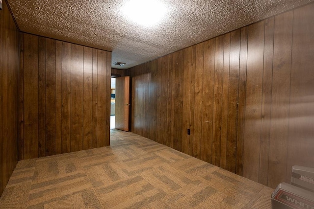 carpeted spare room featuring a textured ceiling and wood walls