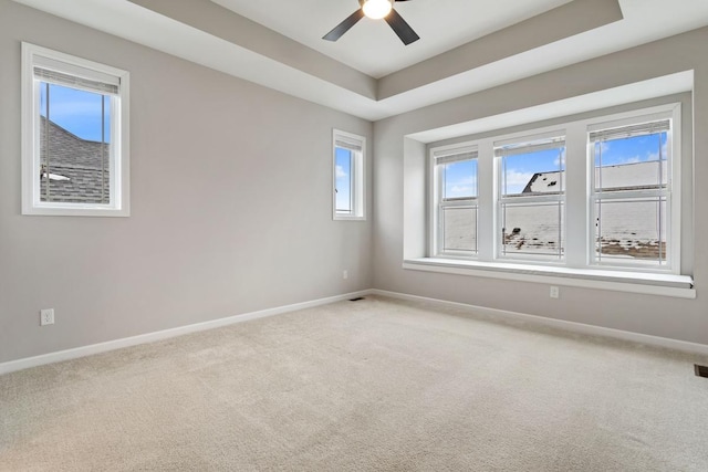 spare room featuring a raised ceiling, ceiling fan, and carpet