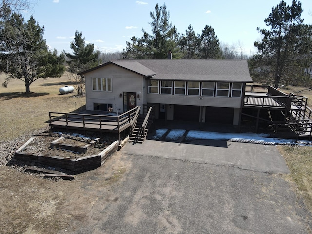back of property featuring roof with shingles, a garage, aphalt driveway, and a wooden deck