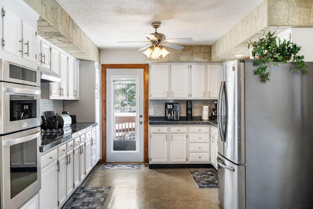 kitchen with appliances with stainless steel finishes, decorative backsplash, dark countertops, white cabinets, and ceiling fan