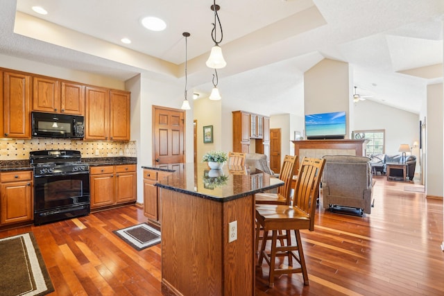 kitchen with open floor plan, black appliances, a tray ceiling, and a breakfast bar