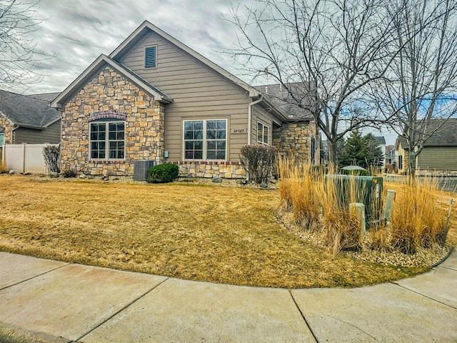 view of front of property featuring stone siding, fence, and cooling unit