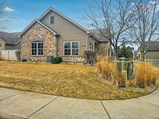 view of front of property featuring stone siding, fence, cooling unit, and a front yard