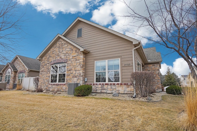 view of front facade with stone siding, fence, a front lawn, and cooling unit