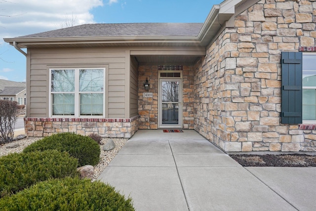 view of exterior entry with stone siding and a shingled roof