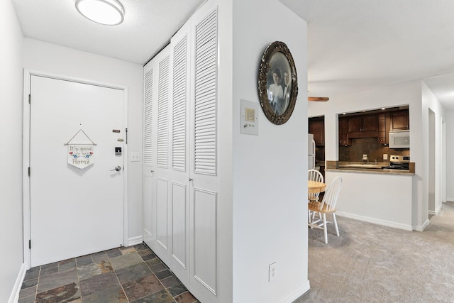 corridor featuring stone finish floor, dark carpet, and baseboards