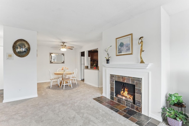 carpeted living room with a tiled fireplace, a ceiling fan, and baseboards