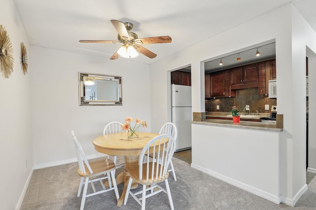 dining space featuring a ceiling fan, light colored carpet, and baseboards