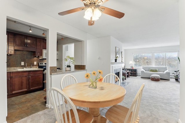 dining area with light colored carpet, a warm lit fireplace, and ceiling fan