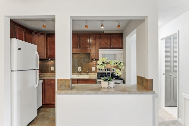 kitchen featuring a sink, backsplash, white appliances, a peninsula, and light countertops