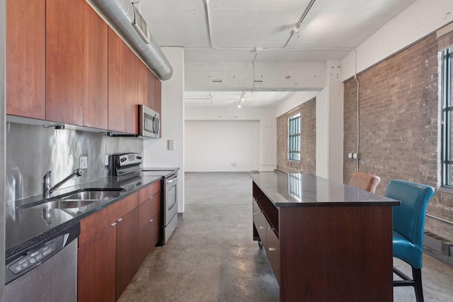 kitchen featuring sink, a breakfast bar area, stainless steel appliances, a kitchen island, and concrete floors