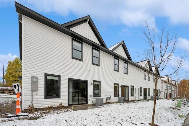 snow covered rear of property featuring central AC unit