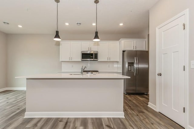 kitchen featuring white cabinetry, appliances with stainless steel finishes, decorative light fixtures, and a center island with sink