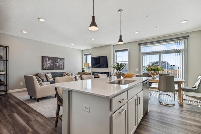 kitchen with dark hardwood / wood-style floors, sink, hanging light fixtures, stainless steel dishwasher, and a center island with sink