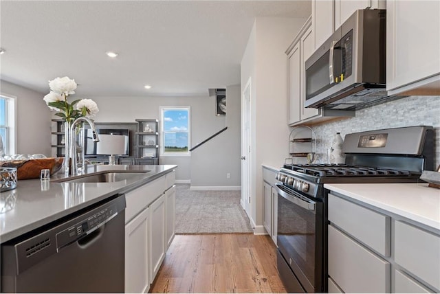 kitchen with appliances with stainless steel finishes, tasteful backsplash, white cabinetry, sink, and light hardwood / wood-style flooring