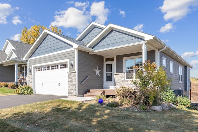 craftsman-style home featuring central air condition unit, an attached garage, a front yard, stone siding, and driveway