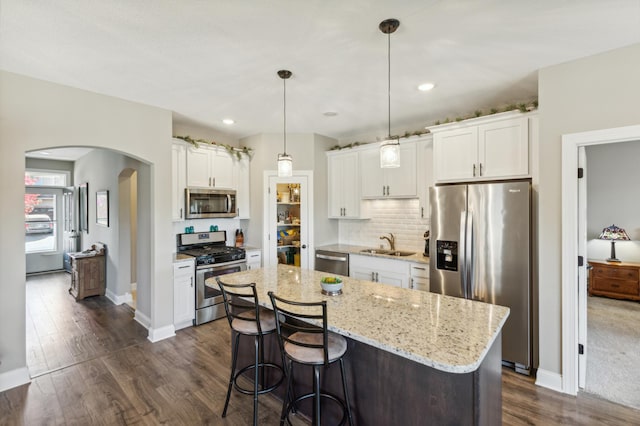 kitchen featuring arched walkways, white cabinets, appliances with stainless steel finishes, dark wood-style flooring, and a sink