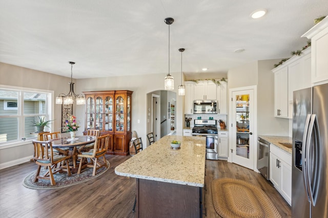 kitchen with arched walkways, white cabinetry, appliances with stainless steel finishes, dark wood-style floors, and pendant lighting