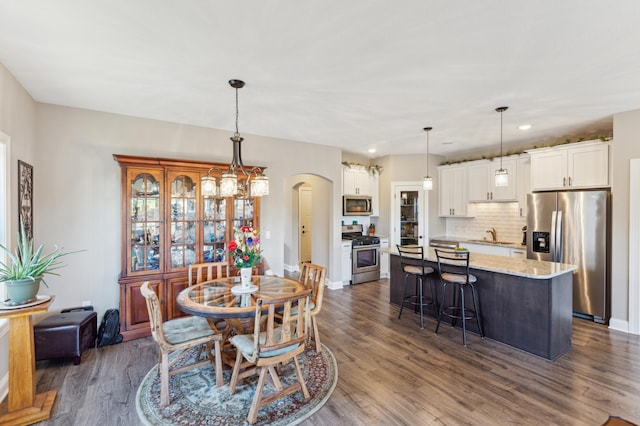 dining room with dark wood-type flooring, arched walkways, baseboards, and recessed lighting