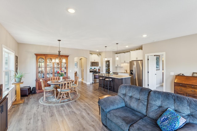 living room featuring arched walkways, light wood-type flooring, baseboards, and recessed lighting