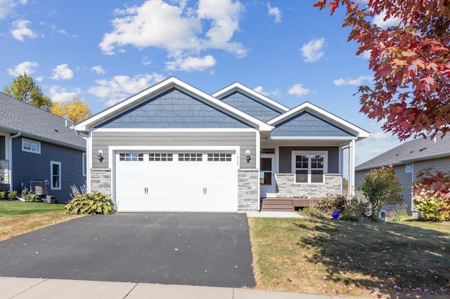 craftsman-style home with a garage, stone siding, aphalt driveway, and a front yard