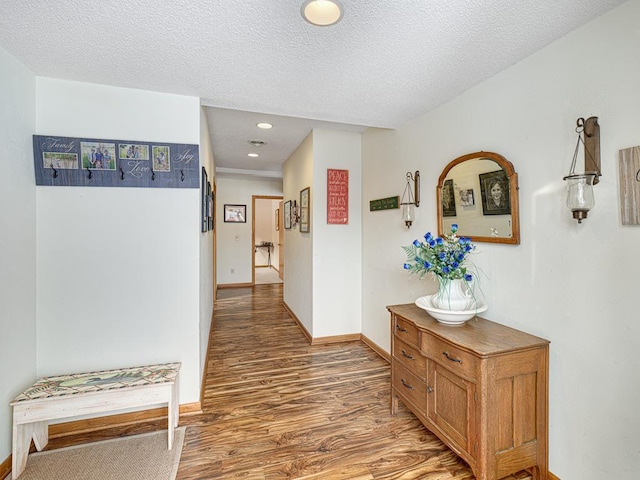 hallway featuring a textured ceiling, baseboards, wood finished floors, and recessed lighting