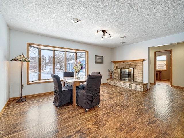 dining space with a wealth of natural light, a brick fireplace, wood finished floors, and visible vents