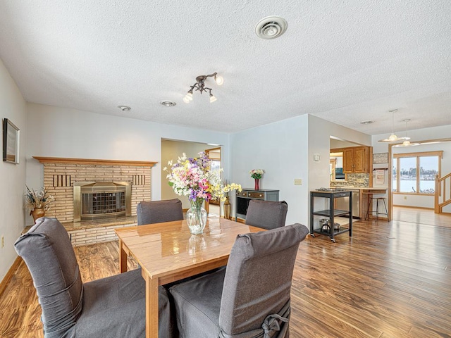 dining room featuring a textured ceiling, a brick fireplace, wood finished floors, and visible vents