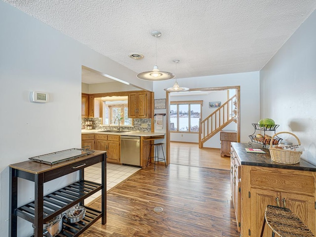 kitchen with light wood-style flooring, a sink, hanging light fixtures, stainless steel dishwasher, and decorative backsplash