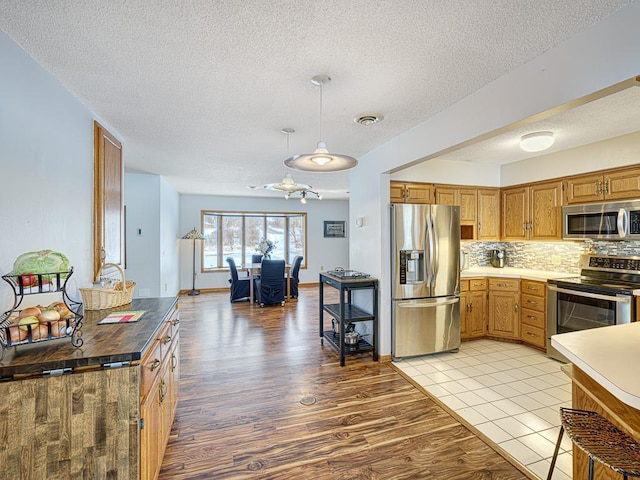 kitchen featuring light wood-style flooring, stainless steel appliances, visible vents, decorative backsplash, and pendant lighting