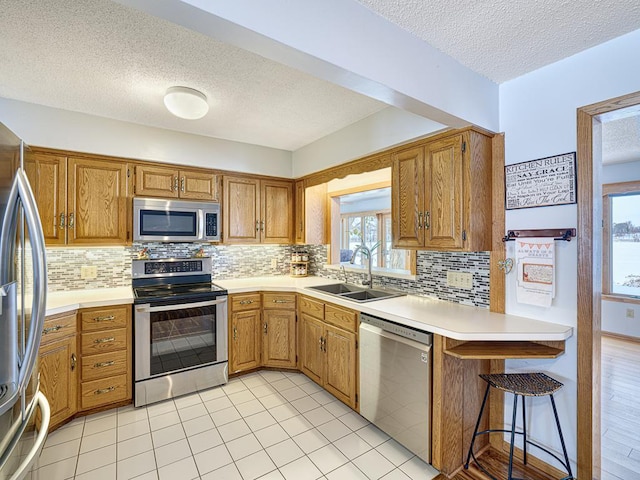 kitchen with light countertops, appliances with stainless steel finishes, brown cabinetry, a sink, and a peninsula