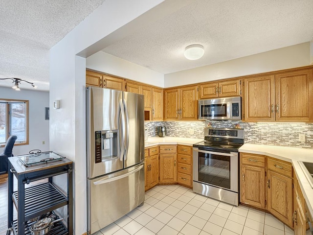 kitchen featuring light tile patterned floors, stainless steel appliances, light countertops, backsplash, and brown cabinetry