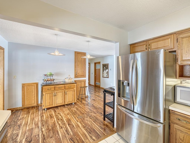 kitchen featuring a textured ceiling, white microwave, light wood-type flooring, stainless steel refrigerator with ice dispenser, and pendant lighting