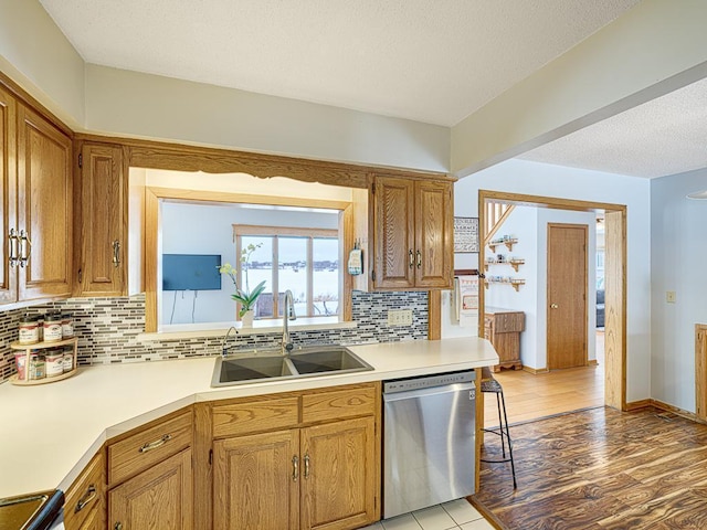 kitchen with a sink, light wood-style floors, light countertops, backsplash, and dishwasher