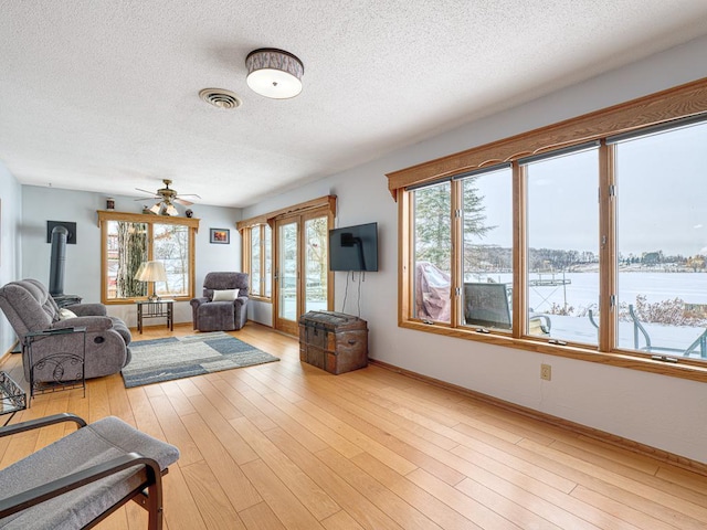 living area with visible vents, light wood-style floors, a wood stove, a textured ceiling, and baseboards