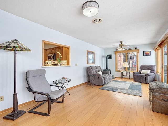 living area featuring visible vents, light wood finished floors, a textured ceiling, and a wood stove