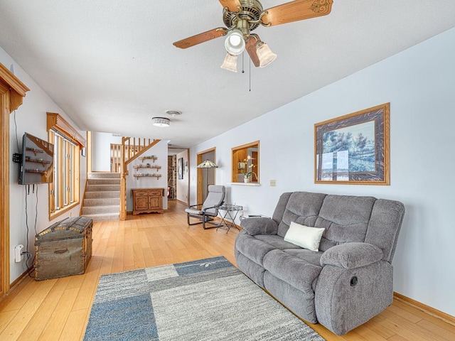 living room featuring a ceiling fan, wood finished floors, baseboards, and stairs