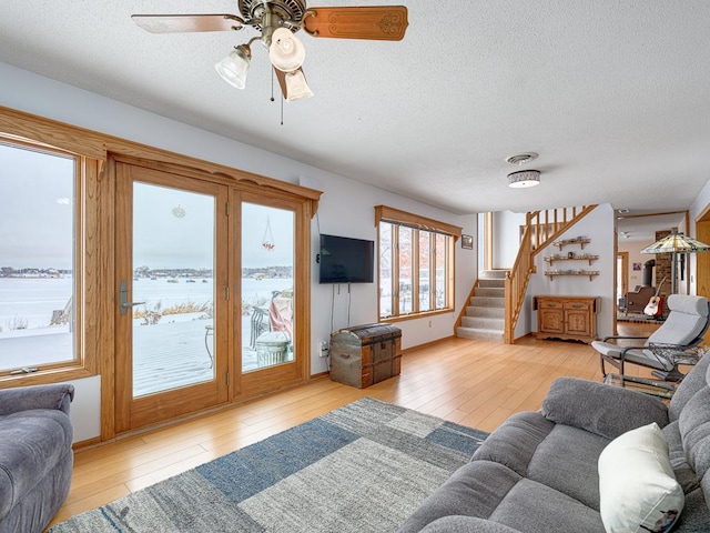 living area with ceiling fan, a textured ceiling, stairway, and wood finished floors