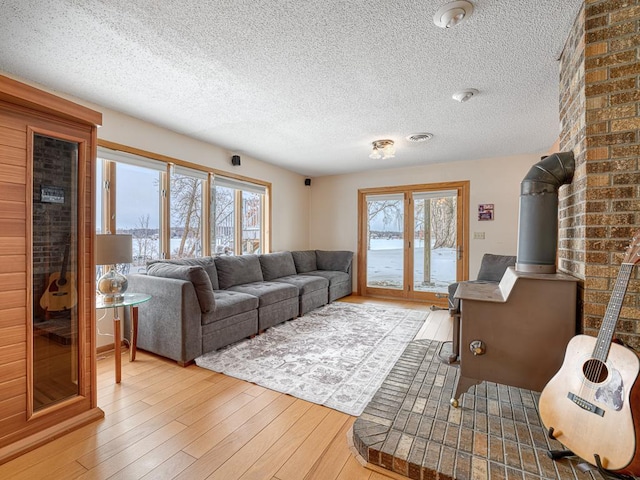 living area with a wood stove, a healthy amount of sunlight, a textured ceiling, and wood finished floors