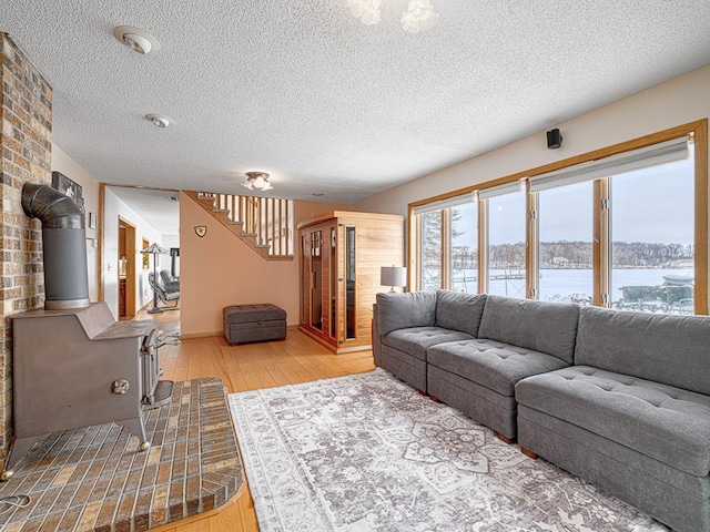 living area with a textured ceiling, a water view, stairs, light wood-type flooring, and a wood stove