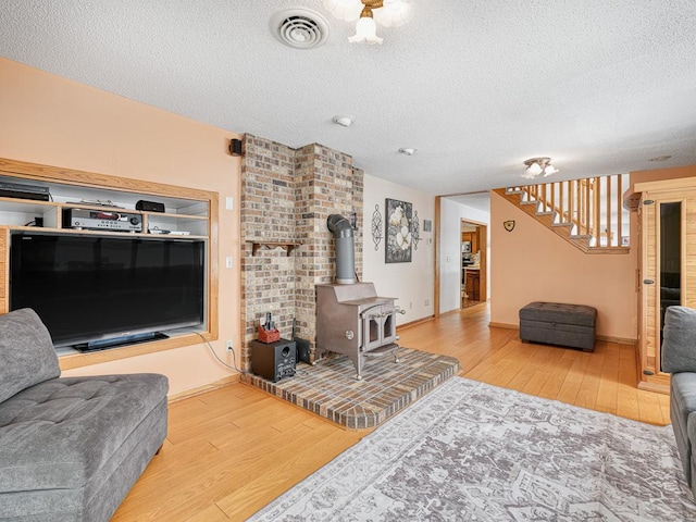 living area featuring visible vents, wood finished floors, a wood stove, stairs, and a textured ceiling