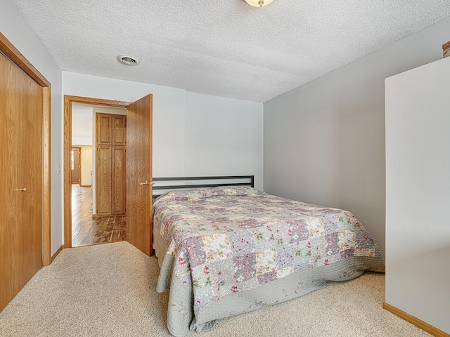 bedroom with a textured ceiling, light colored carpet, visible vents, baseboards, and a closet