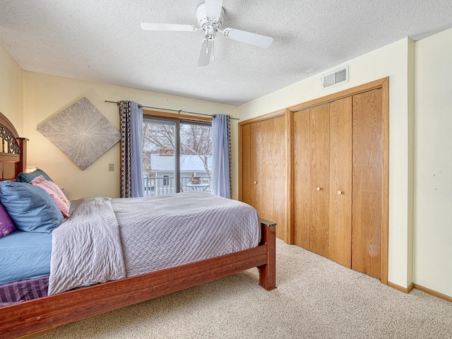 carpeted bedroom featuring ceiling fan, a textured ceiling, visible vents, and multiple closets