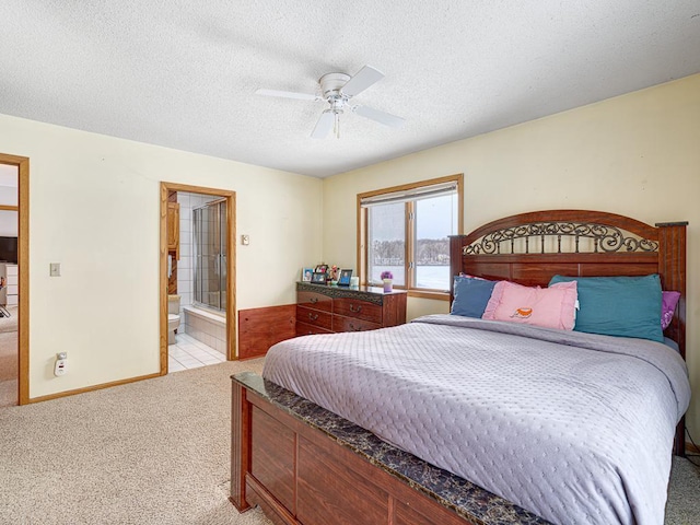 bedroom featuring baseboards, light colored carpet, ensuite bath, ceiling fan, and a textured ceiling