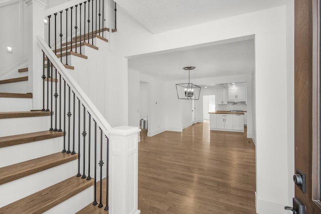 stairs with wood-type flooring and a chandelier