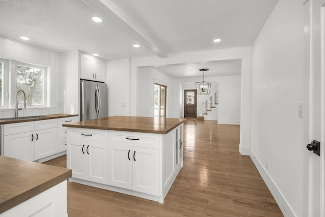 kitchen with wooden counters, stainless steel fridge, and white cabinets