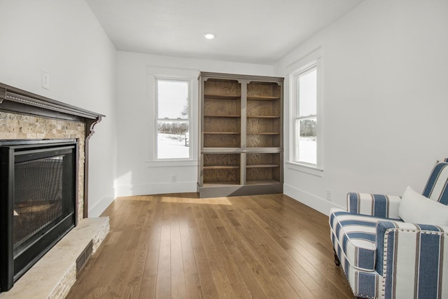 sitting room with wood-type flooring, a stone fireplace, and a healthy amount of sunlight