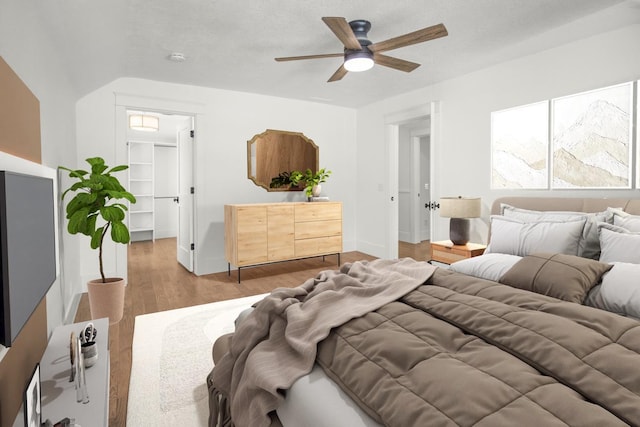 bedroom with a walk in closet, hardwood / wood-style floors, a textured ceiling, and ceiling fan