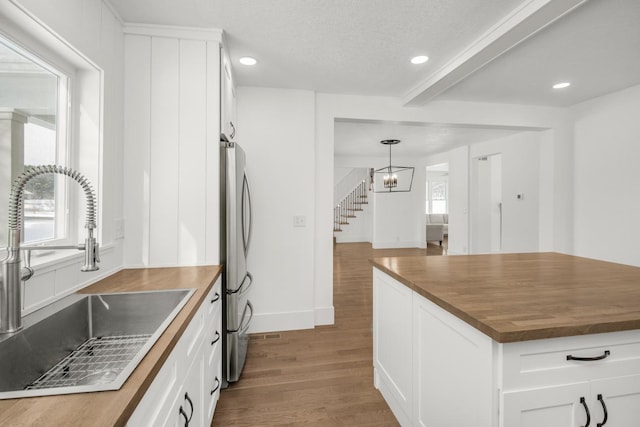 kitchen with white cabinetry, a sink, butcher block counters, recessed lighting, and wood finished floors