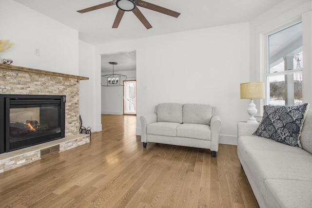 living room featuring ceiling fan, a stone fireplace, visible vents, baseboards, and wood finished floors